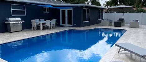 A swimming pool with lounge chairs, a barbecue grill, and a covered patio area.
