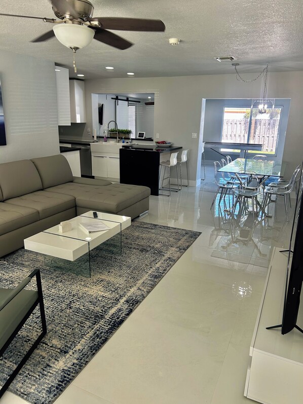 A modern living room with a sofa, coffee table, and a dining area with chairs and a table. - Family-Friendly 4BR with Pool & Game Room, 5 Mins to Beach! (Deerfield Beach)