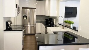 A modern kitchen with white cabinetry, stainless steel appliances, a black countertop, and a built-in island with bar stools.