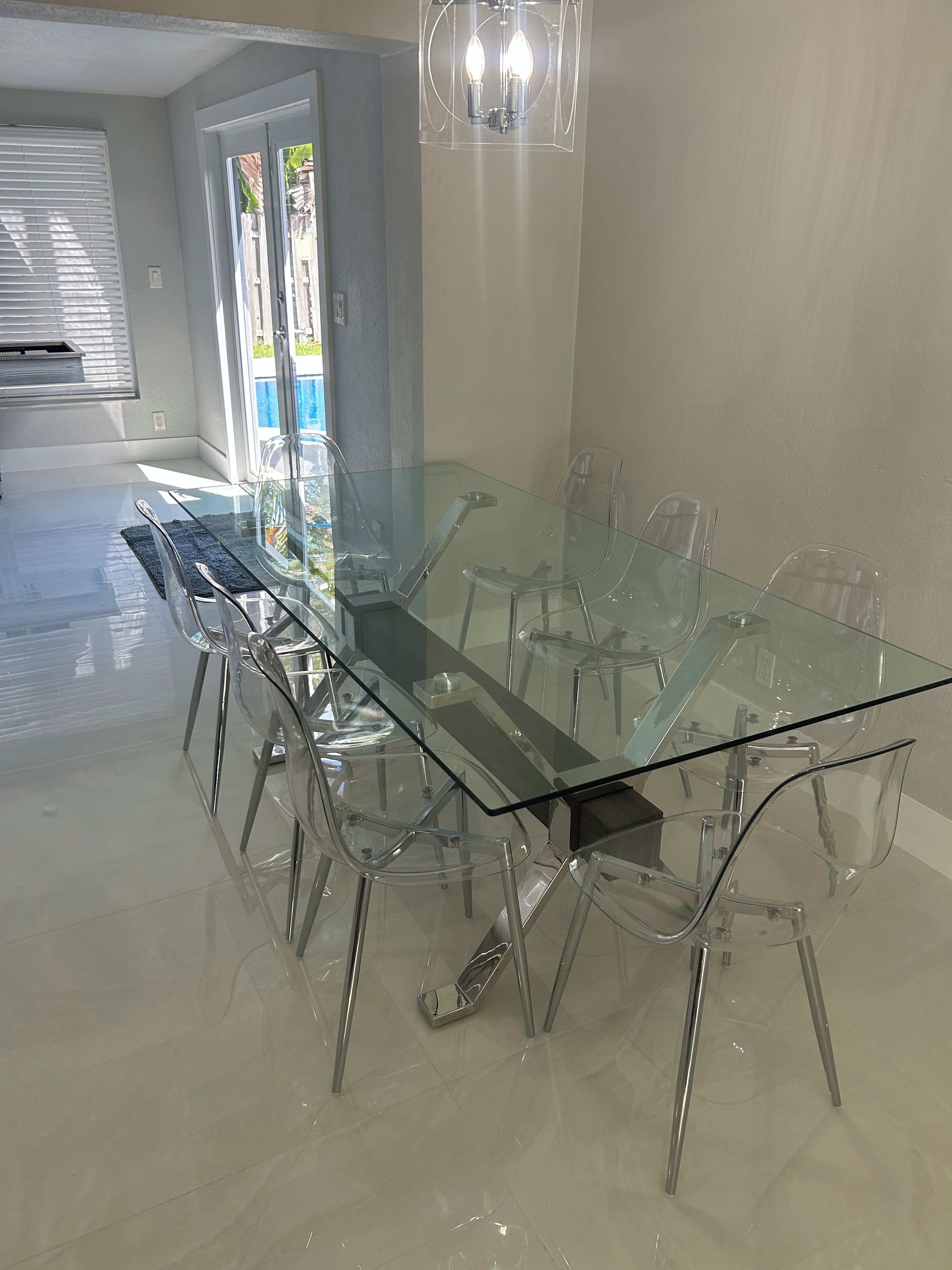 A modern dining area with a glass table and chairs, a chandelier, and a view of the outdoors.