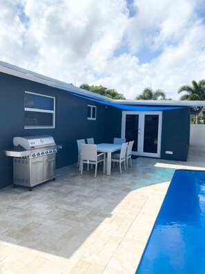 A backyard with a barbecue grill, a dining table with chairs, and a swimming pool.