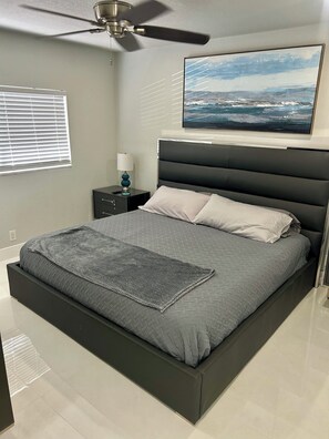 A modern bedroom with a bed, a nightstand, a lamp, a ceiling fan, and a painting on the wall.