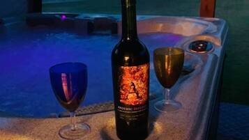 A hot tub with a bottle of wine and two glasses on a countertop.
