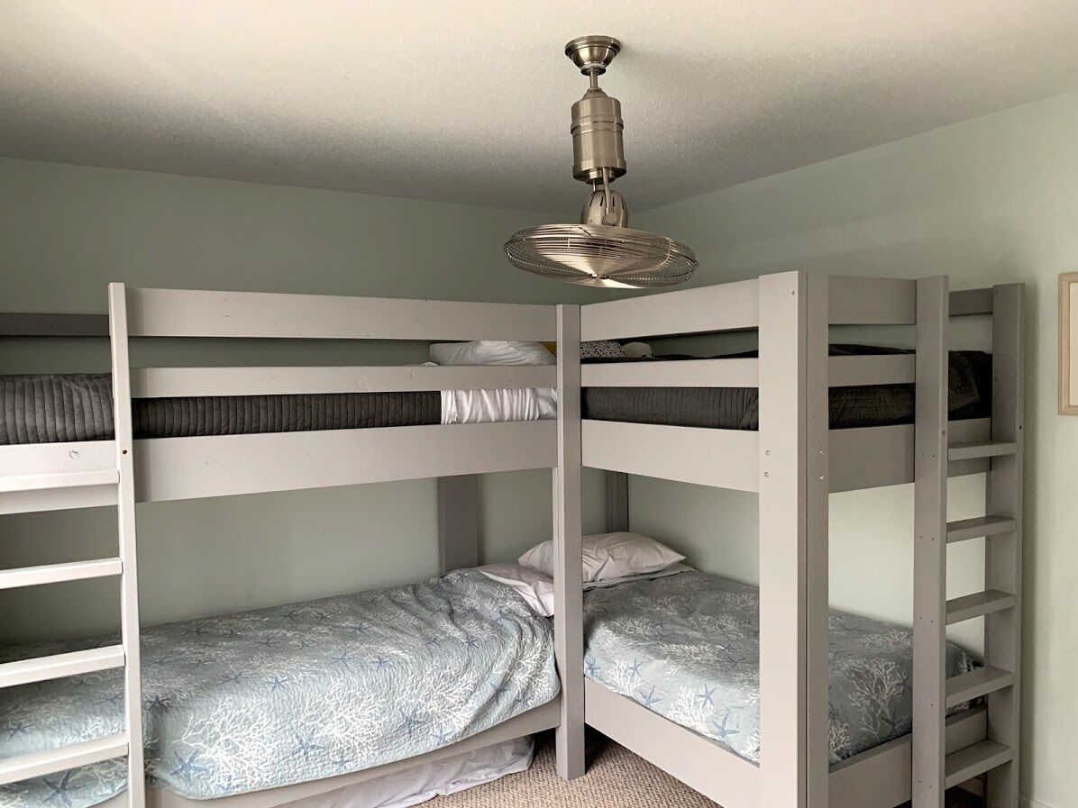 Une chambre avec un lit superposé, un ventilateur de plafond, des murs blancs et un sol recouvert de moquette.