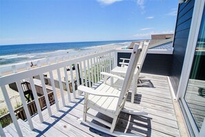 Eine Holzterrasse mit weißer Geländer, die auf einen Strand blickt.
