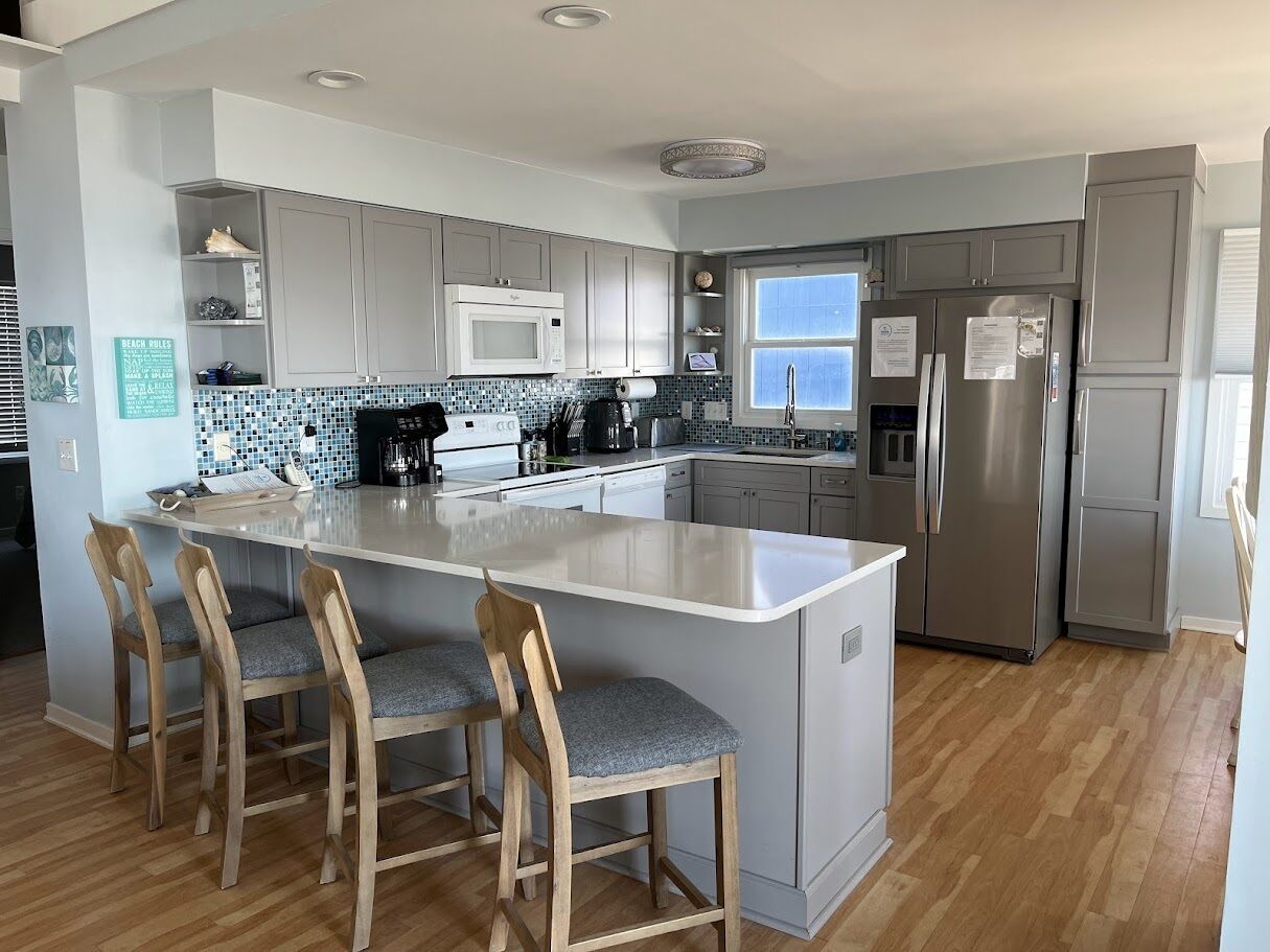 A modern kitchen with a central island, bar stools, stainless steel appliances, and a tiled backsplash.