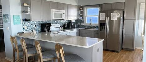 A modern kitchen with a central island, bar stools, stainless steel appliances, and a tiled backsplash.