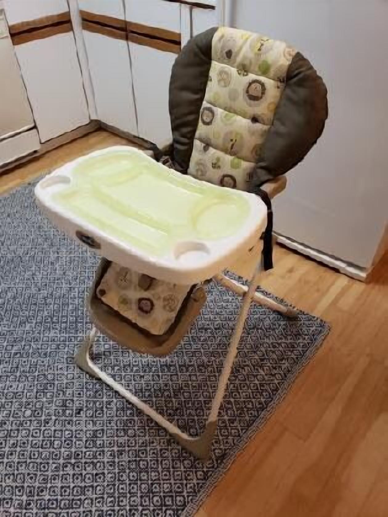 A baby high chair with a patterned cushion, a tray, and a metal frame.