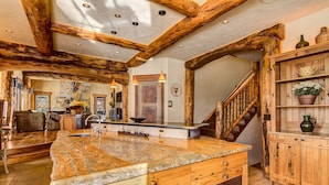 A rustic kitchen with a large island, wooden beams, and a stone backsplash. - Rustic-elegance wrapped in custom mountain luxury, steps from Baldy Hiking Trail and shuttle stop (Breckenridge)