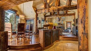 A spacious interior with a wooden staircase leading to a seating area, a kitchen in the background, and large windows providing natural light. - Rustic-elegance wrapped in custom mountain luxury, steps from Baldy Hiking Trail and shuttle stop (Breckenridge)
