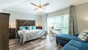 Ein Schlafzimmer mit einem Bett, einem Schreibtisch, einem Stuhl, einem blauen Sofa und einem Deckenventilator.