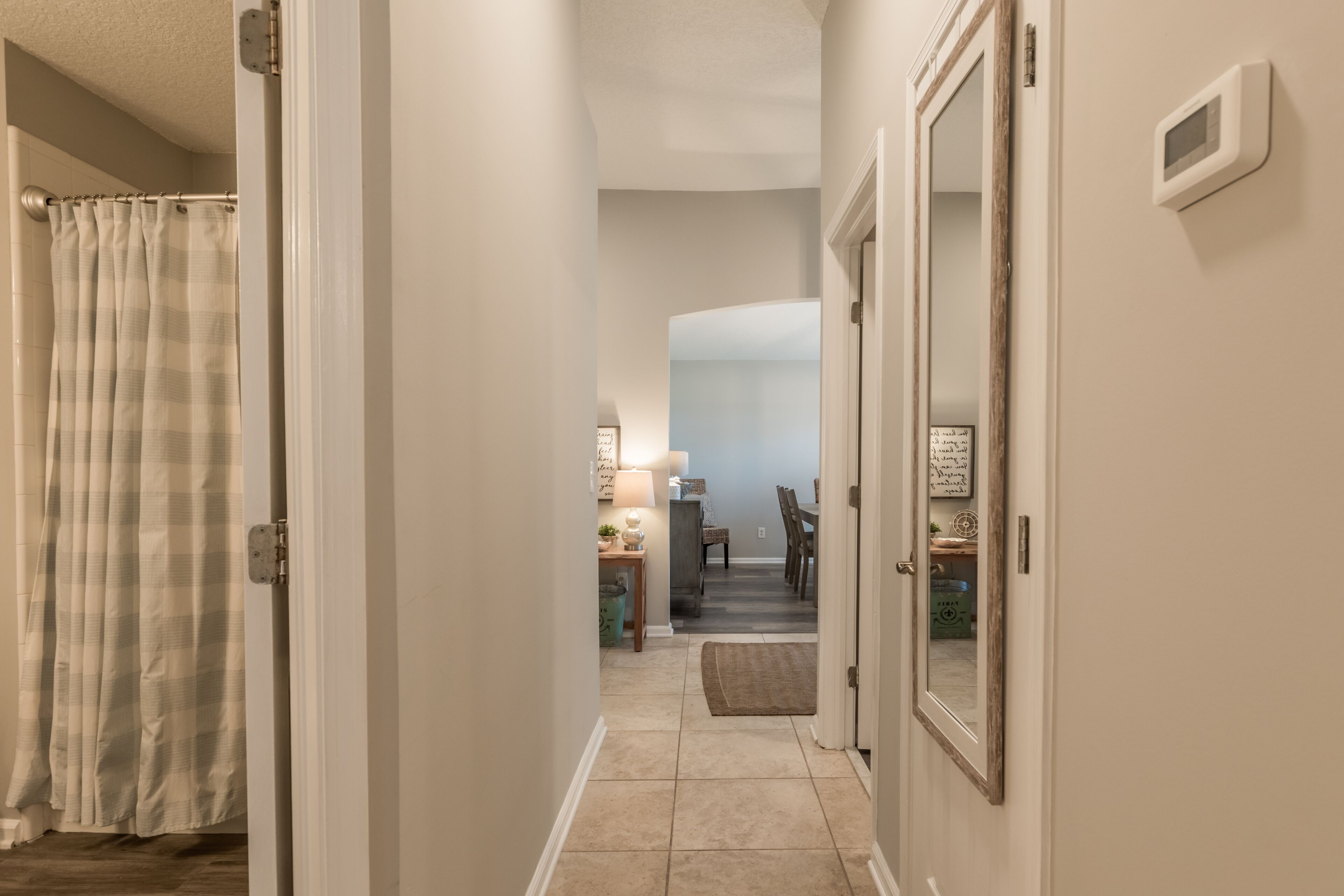 A hallway with a shower curtain, a mirror, and a door leading to a dining area.