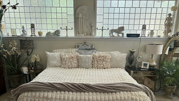 A bedroom with a large bed, a window with decorative items, and a dresser with a mirror.