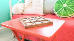 A bed with a red quilt, a pillow with a bird design, and a wooden tray with white objects on a small orange table.