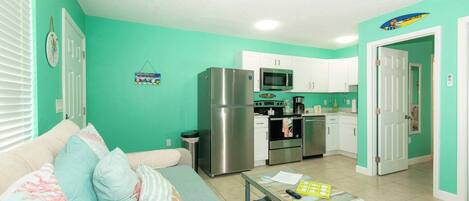 Un espacio habitable compacto con kitchenette, un sofá con cojines estampados y una pequeña mesa con papeles y un control remoto.