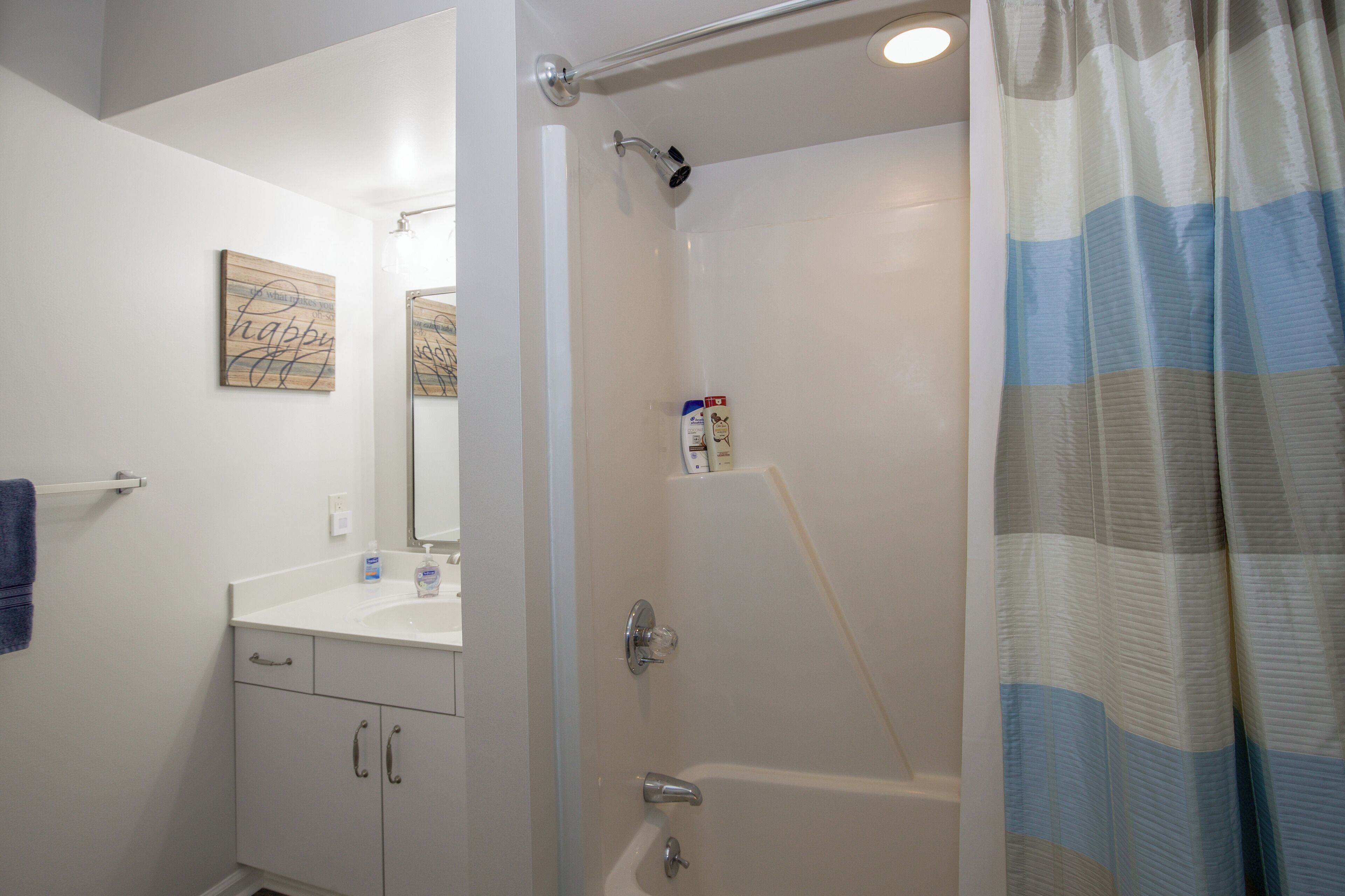 A bathroom with a white sink, a mirror, a shower with a glass door, and a blue-striped shower curtain.