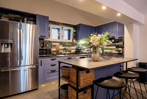 A modern kitchen with a stainless steel refrigerator, a central island with stools, and a decorative vase with flowers.