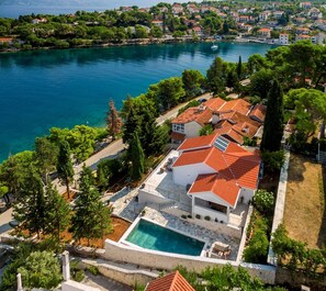 A coastal property with a swimming pool, red-tiled roofs, and a view of the sea.