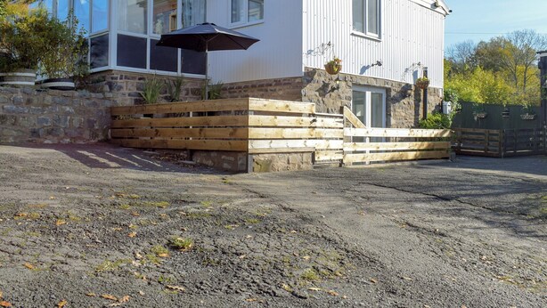 Kaksikerroksinen talo, jossa on kivinen pohjarakenne, puinen terassi ja suuri lasi-ikkuna.
