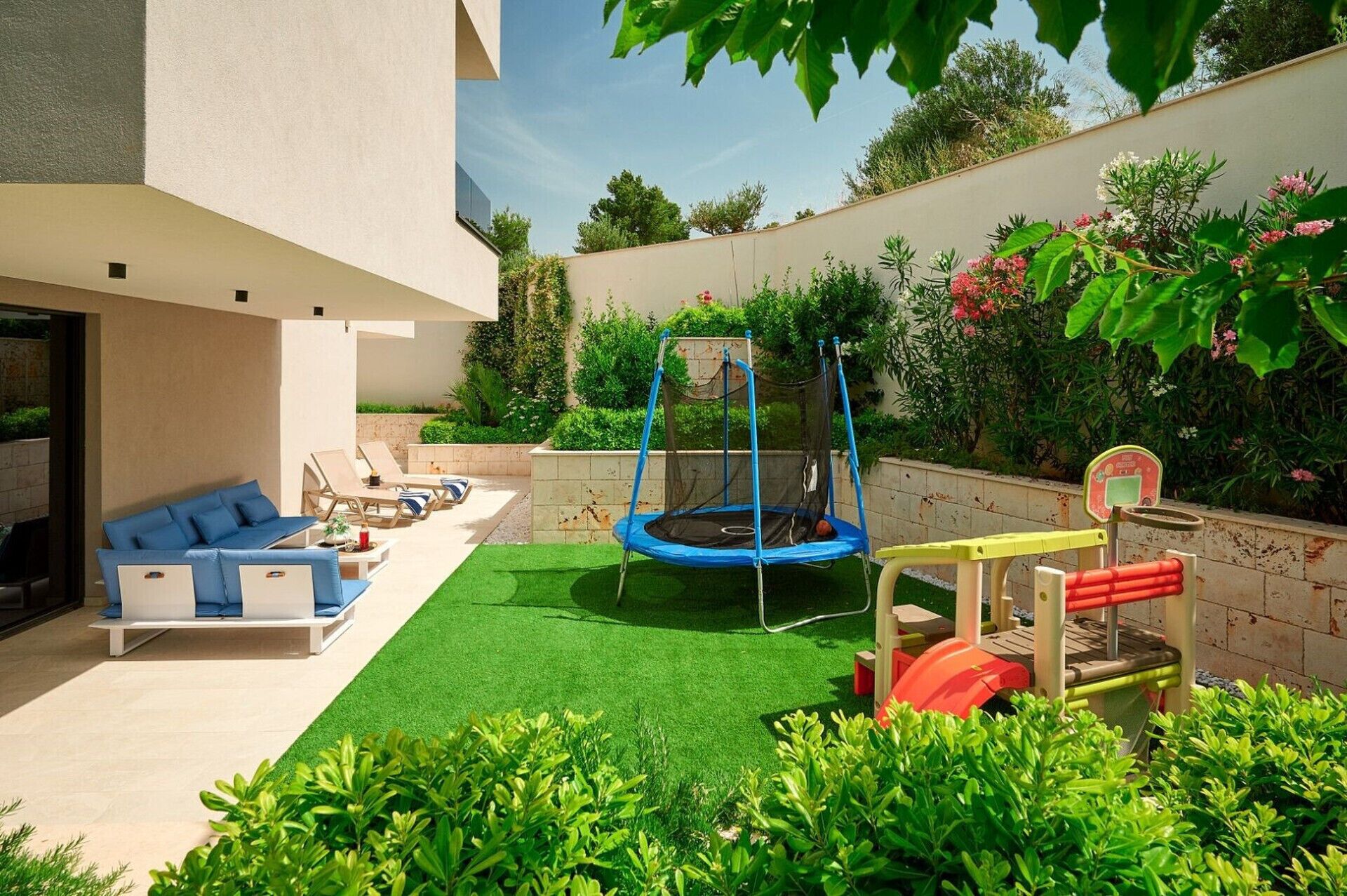 A modern outdoor living area with a trampoline, playset, and a sofa set.