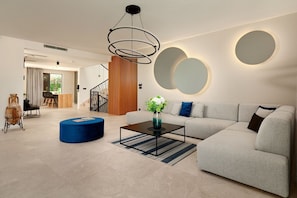 Un salon moderne avec un canapé d’angle, une table basse et un pouf bleu.