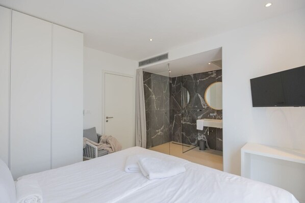 Quarto de hotel moderno com uma cama grande, um closet espaçoso, banheiro com chuveiro de mármore e televisão na parede.