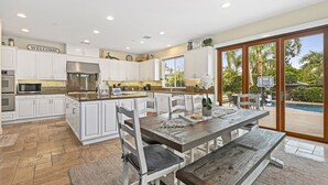 A spacious kitchen with white cabinetry, a central island, and a dining area with a wooden table and benches. - Luxury Family Resort Home Near Beach~ Pool ~ Hot Tub ~ Sportcourt (Encinitas)