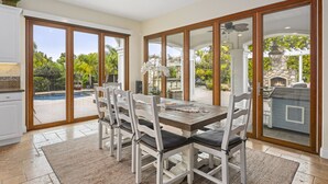 A dining area with a table and chairs, a view of a pool, and a stone fireplace. - Luxury Family Resort Home Near Beach~ Pool ~ Hot Tub ~ Sportcourt (Encinitas)