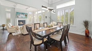 A spacious living room with a large wooden dining table, beige sofas, and a fireplace. - Luxury Family Resort Home Near Beach~ Pool ~ Hot Tub ~ Sportcourt (Encinitas)