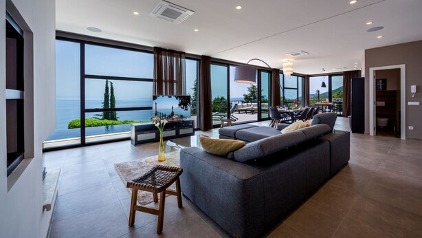 A modern living room with a large sofa, a small table, and a view of the sea. - Luxury Villa Opatija Sapphire with Infinity Pool (Opatija)