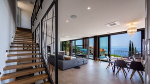 A modern interior with a staircase, a living area with a sofa and chairs, and large windows offering a view of the sea. - Luxury Villa Opatija Sapphire with Infinity Pool (Opatija)