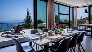 A dining area with a view of the sea, large windows, and modern furniture. - Luxury Villa Opatija Sapphire with Infinity Pool (Opatija)