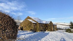 A stone building with a snow-covered roof, surrounded by snow-covered ground and a clear blue sky. - Roosters Rest - UK31826 (Barley, near Clitheroe)