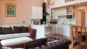 A modern living room with a sofa, a leather ottoman, and a dining area with wooden chairs. - Roosters Rest - UK31826 (Barley, near Clitheroe)