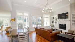 A spacious living room with a wooden floor, a brown leather sofa, a dining table with chairs, and a fireplace. - 600 Linden: 8  BR, 5.5  BA House in Pinehurst, Sleeps 20 (Pinehurst)