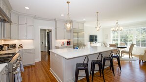 A spacious kitchen with white cabinetry, a large island with bar stools, and a dining area with a round table and chairs. - 600 Linden: 8  BR, 5.5  BA House in Pinehurst, Sleeps 20 (Pinehurst)