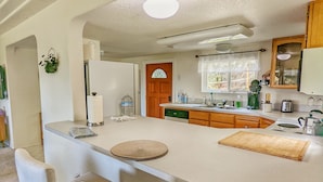 A kitchen with a central island, bar stools, a refrigerator, a sink, and a window with a view.