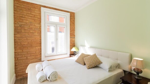 Ein Hotelzimmer mit Backsteinwand, einem großen Fenster, einem Bett mit weißen Leinentüchern und zwei Nachttischlampen.