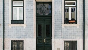 Eine Gebäudefassade mit einer zentralen grünen Tür, blauen und weißen Ziegeln mit Muster und zwei Fenstern mit Balkonen.