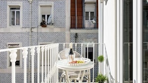 Un balcon avec une table blanche dressée pour deux personnes, une bouteille de champagne et une assiette de fruits.