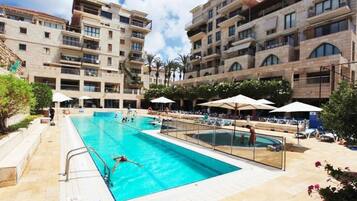 A swimming pool area with multiple pools, surrounded by buildings with balconies and outdoor seating.