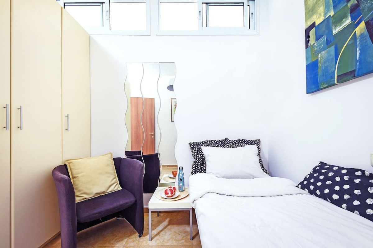 Une chambre à coucher avec un lit, une chaise, une petite table et un tableau accroché au mur.