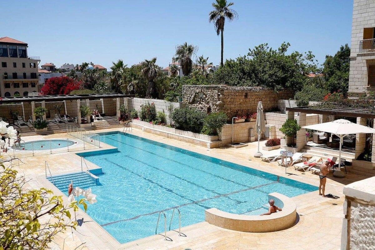 Une piscine dotée d’une terrasse ensoleillée, de chaises longues et d’un mur en pierre.