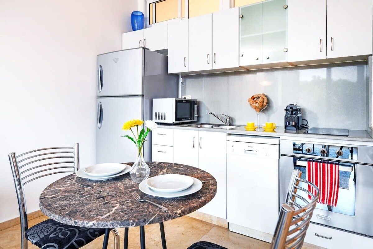 A compact kitchen with white cabinets, a microwave, a coffee maker, and a stove.
