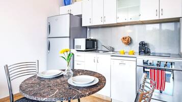 A compact kitchen with white cabinets, a microwave, a coffee maker, and a stove.