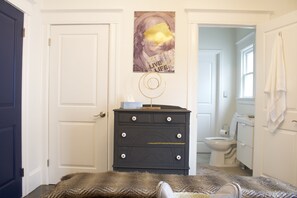 A bedroom with a bed, a dresser, a poster on the wall, and a bathroom visible through an open door.