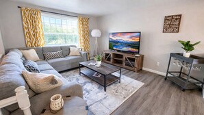 Una sala de estar moderna con un sofá gris, una mesa de centro y un televisor sobre un mueble de madera.