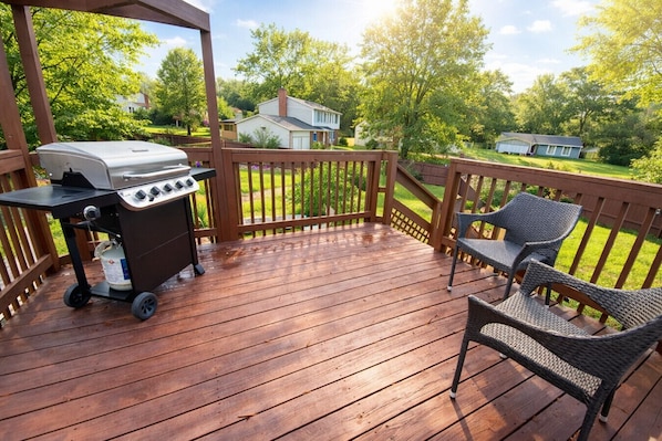 A wooden deck with a grill and wicker chairs.