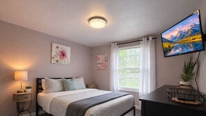 Un dormitorio moderno con cama, mesitas de noche, televisión y ventana con cortinas.