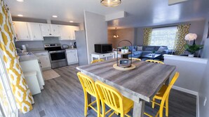 Una cocina moderna con armarios blancos, horno empotrado y comedor con mesa de madera y sillas amarillas.